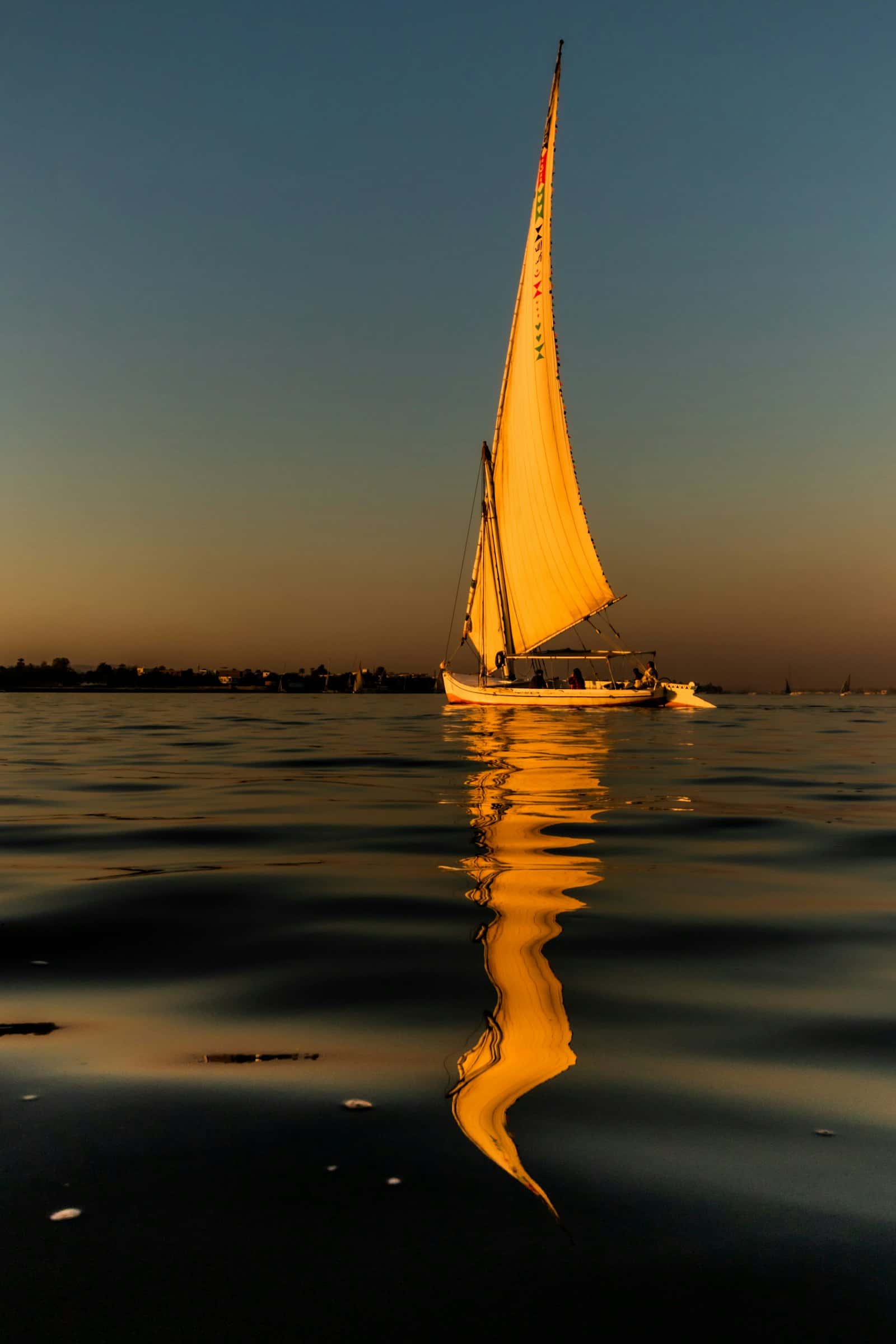 A felucca sailing on the Nile at Luxor, reflected in the water