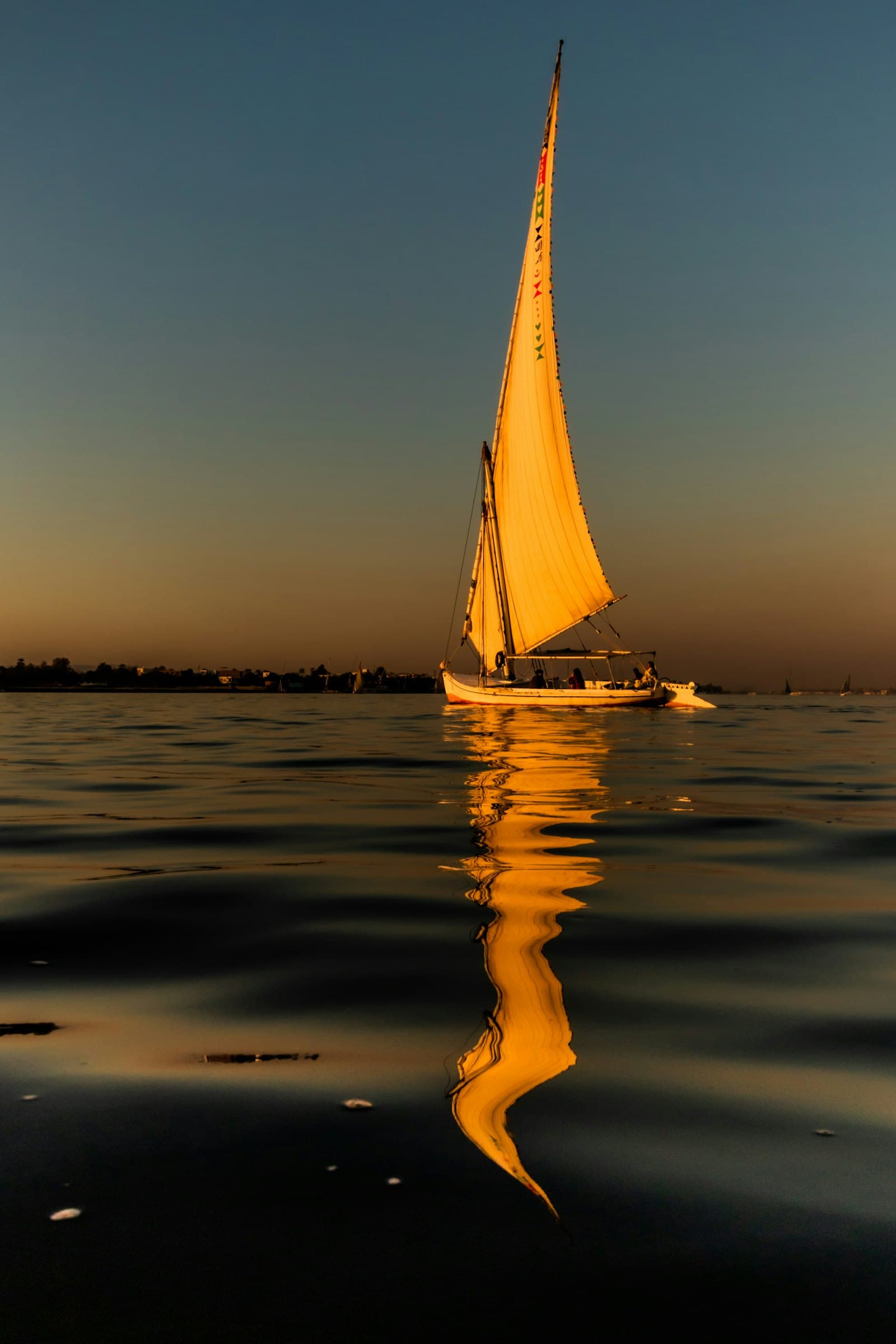 Una falúa navegando por el Nilo en Luxor, reflejada en el agua
