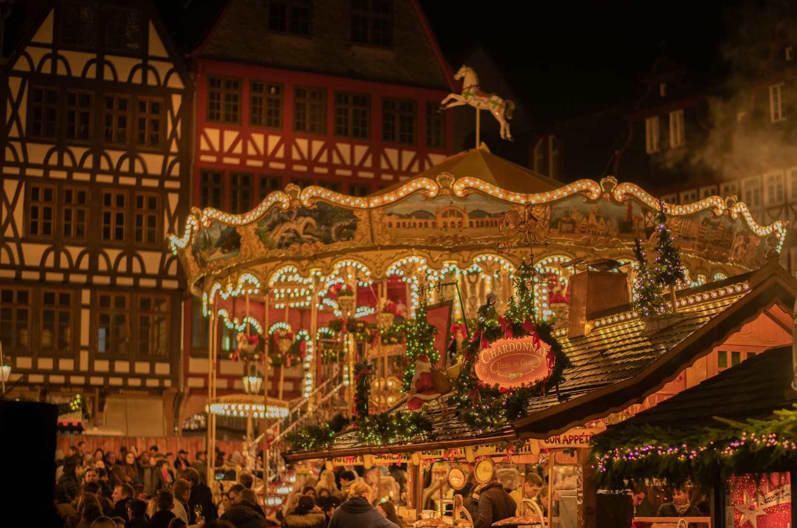Illuminated carousel at a Christmas market in front of half-timbered houses at night